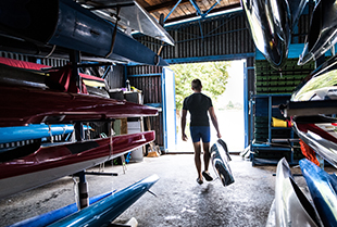 Man carrying a kayak out of a storage unit filled with kayaks